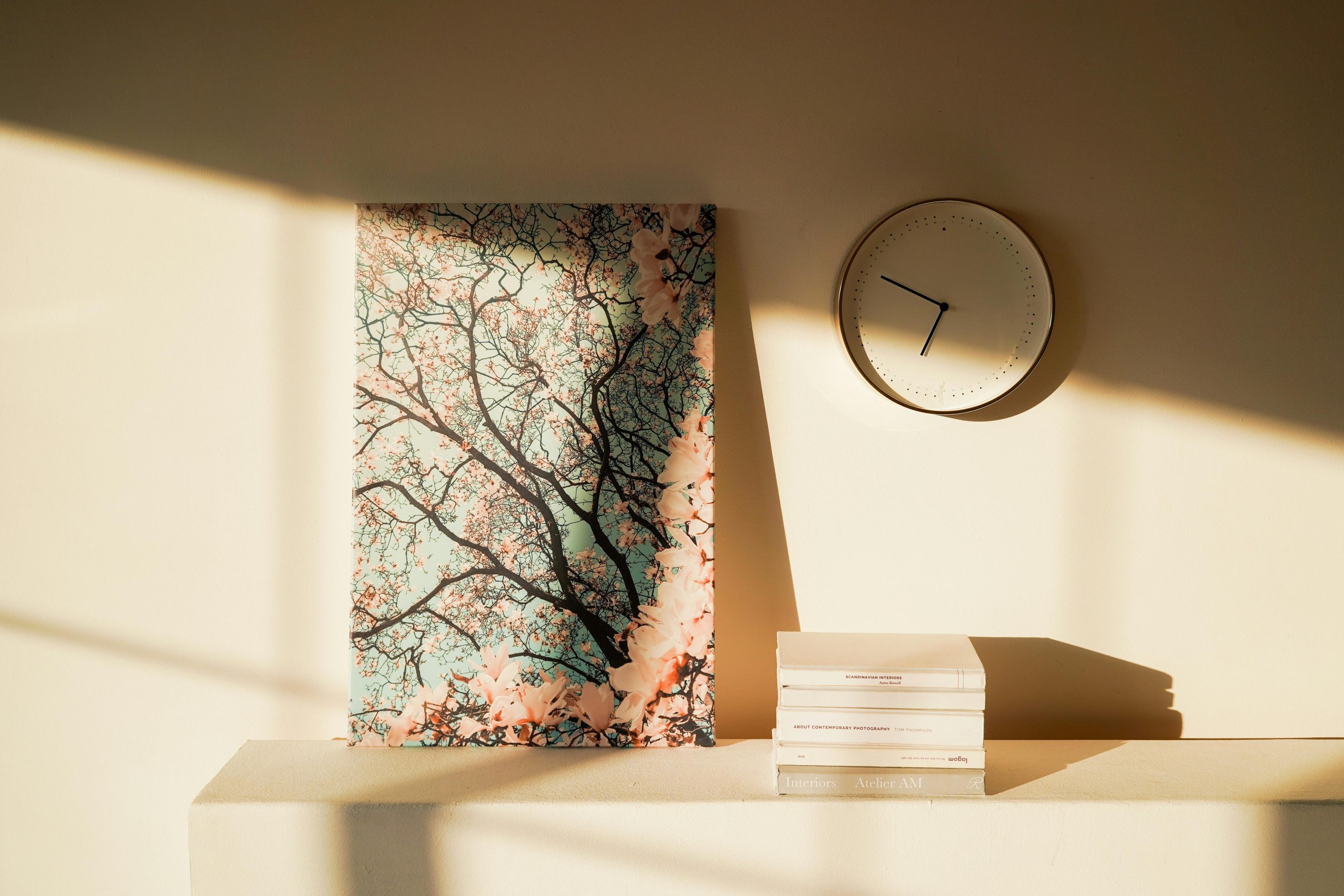 Minimalist wall decor featuring an abstract painting, clock, and soft shadows on a beige wall.